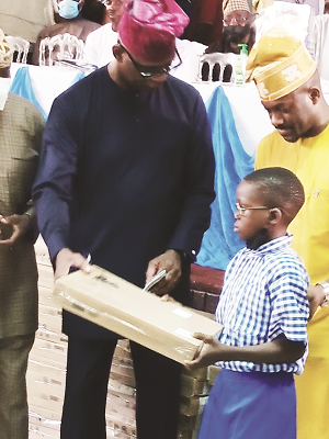 Shasore left Obanikoro presenting a laptop to a pupil of the Eti Osa Community Junior Secondary School Oduwole Mahdi Oladipupo